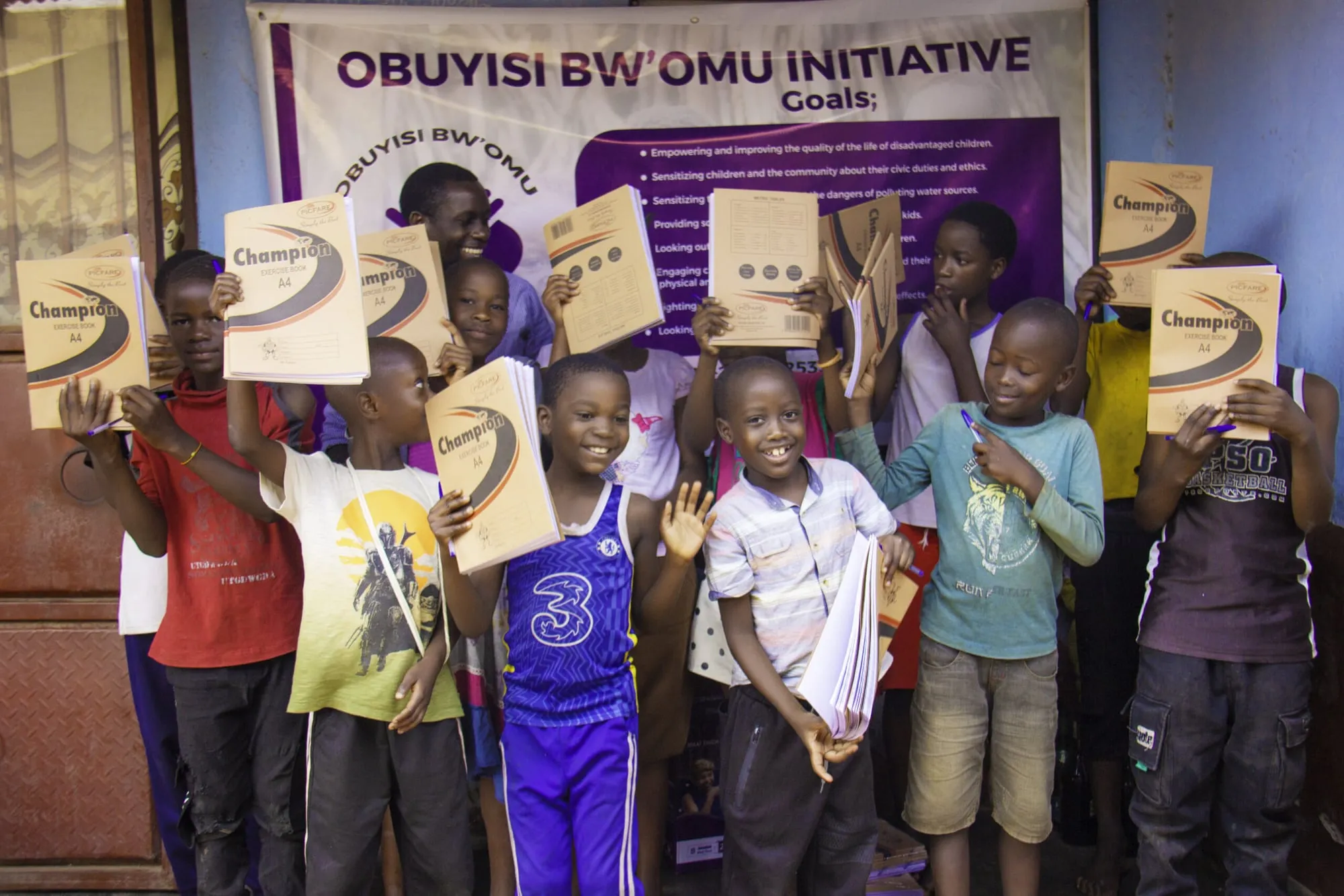 Children in Bwaise proudly holding up new exercise books at an Obuyisi bw'Omu Initiative distribution